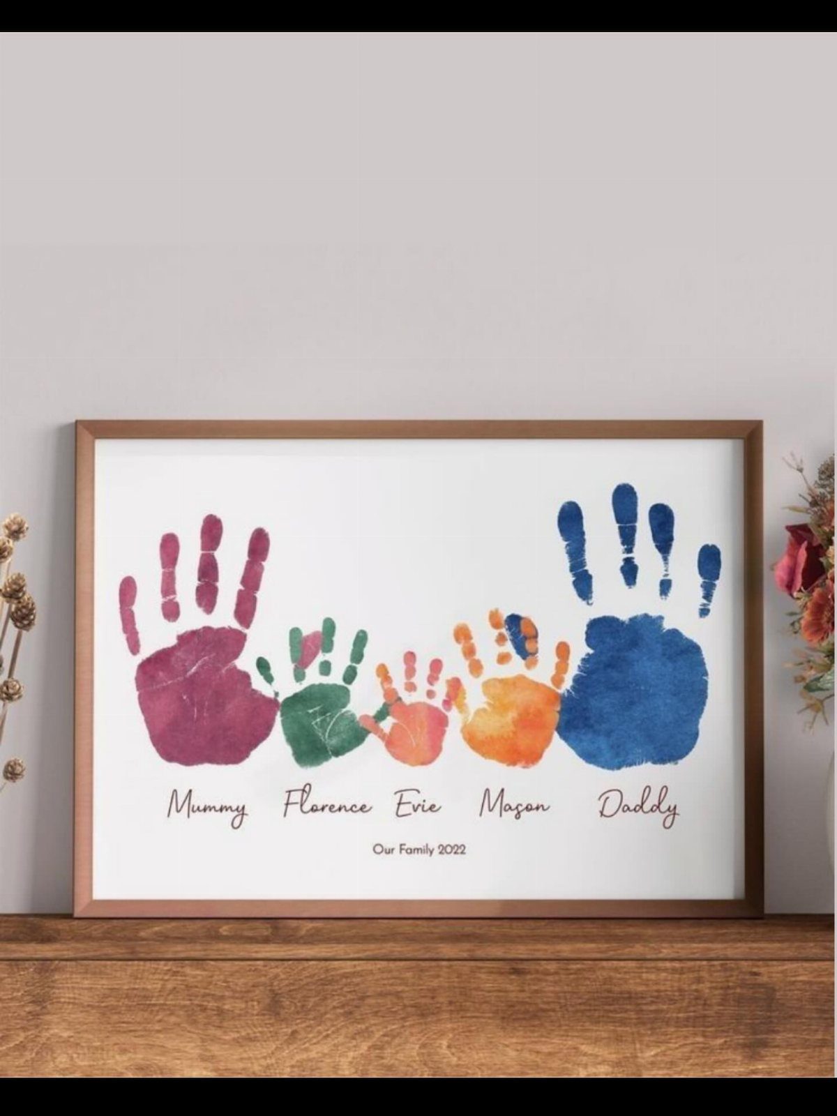 Framed family handprint art with colorful paint prints and names on white background.