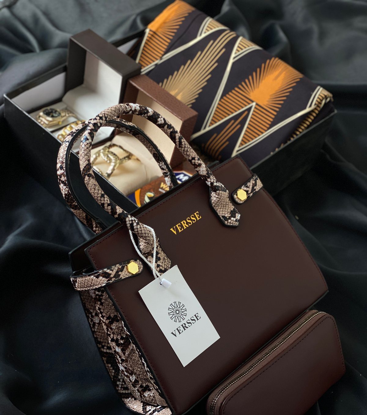 Brown leather handbag and wallet with jewelry and fabric on dark satin cloth
