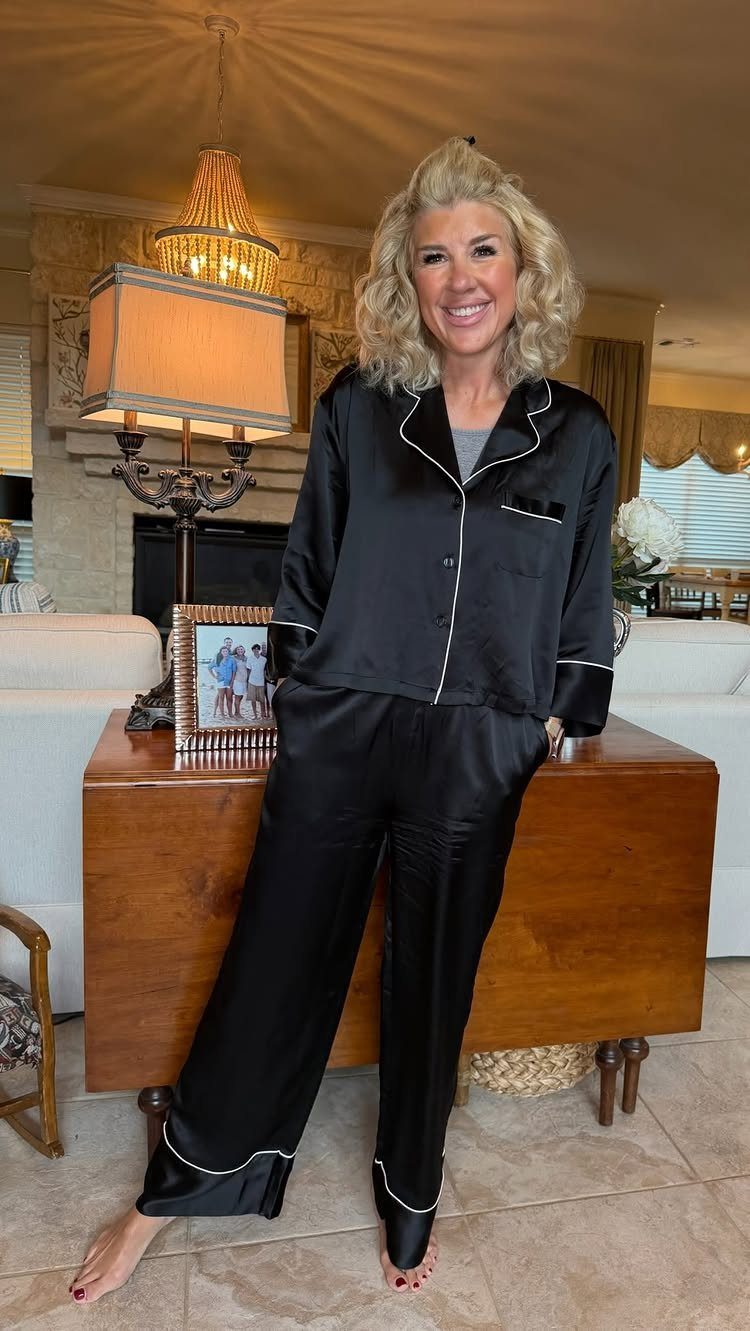 Woman wearing black satin pajamas with white piping standing in a living room.
