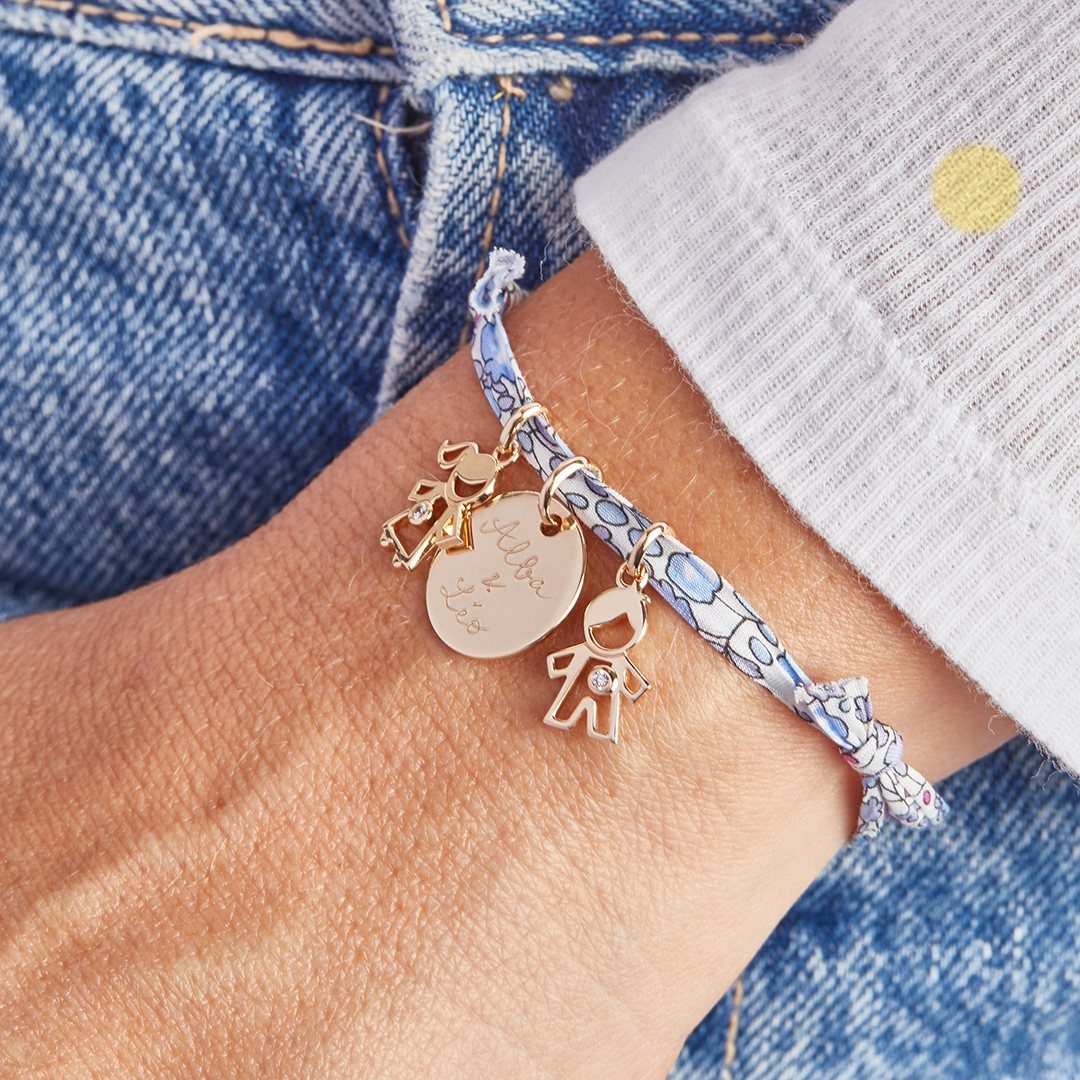 Personalized gold charm bracelet with names and child figures on a wrist