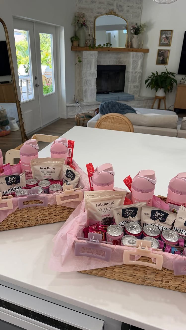 Two woven gift baskets filled with pink water bottles and various packaged snacks.