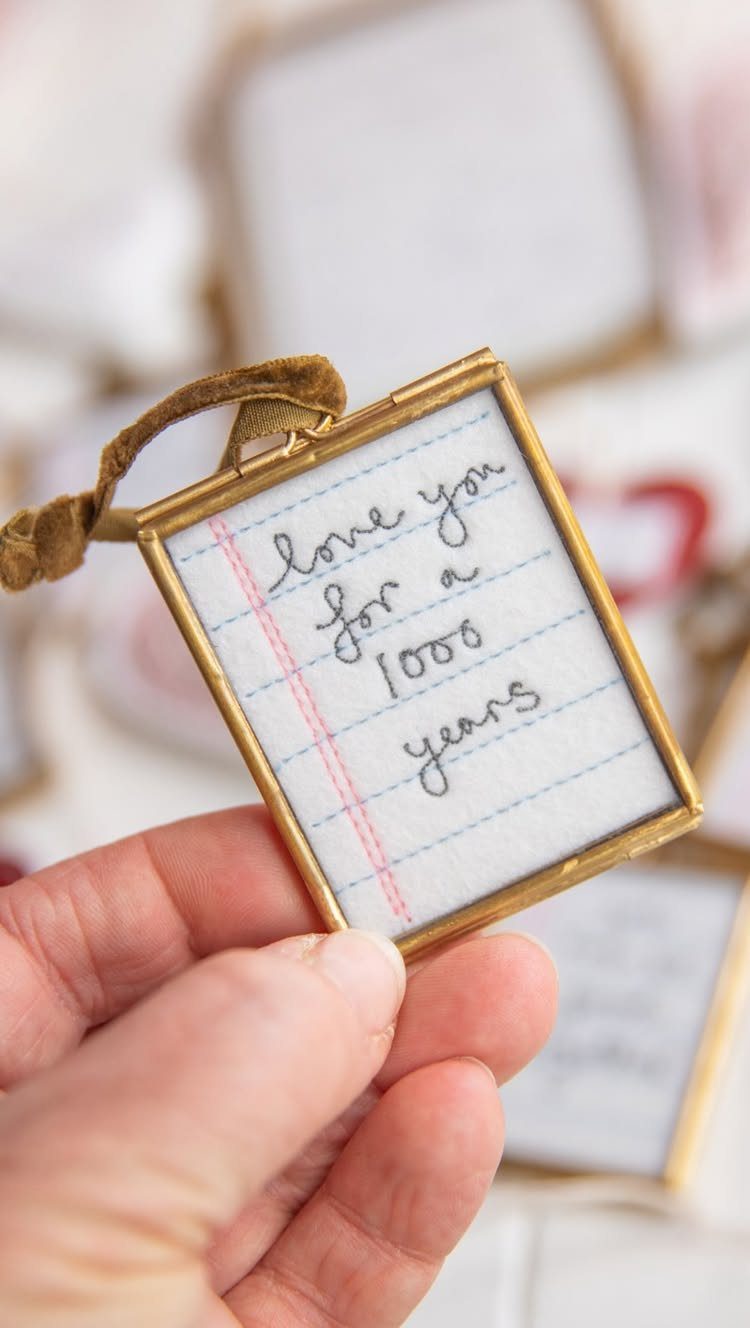 Hand holding a small gold-framed embroidery piece with a handwritten love message.
