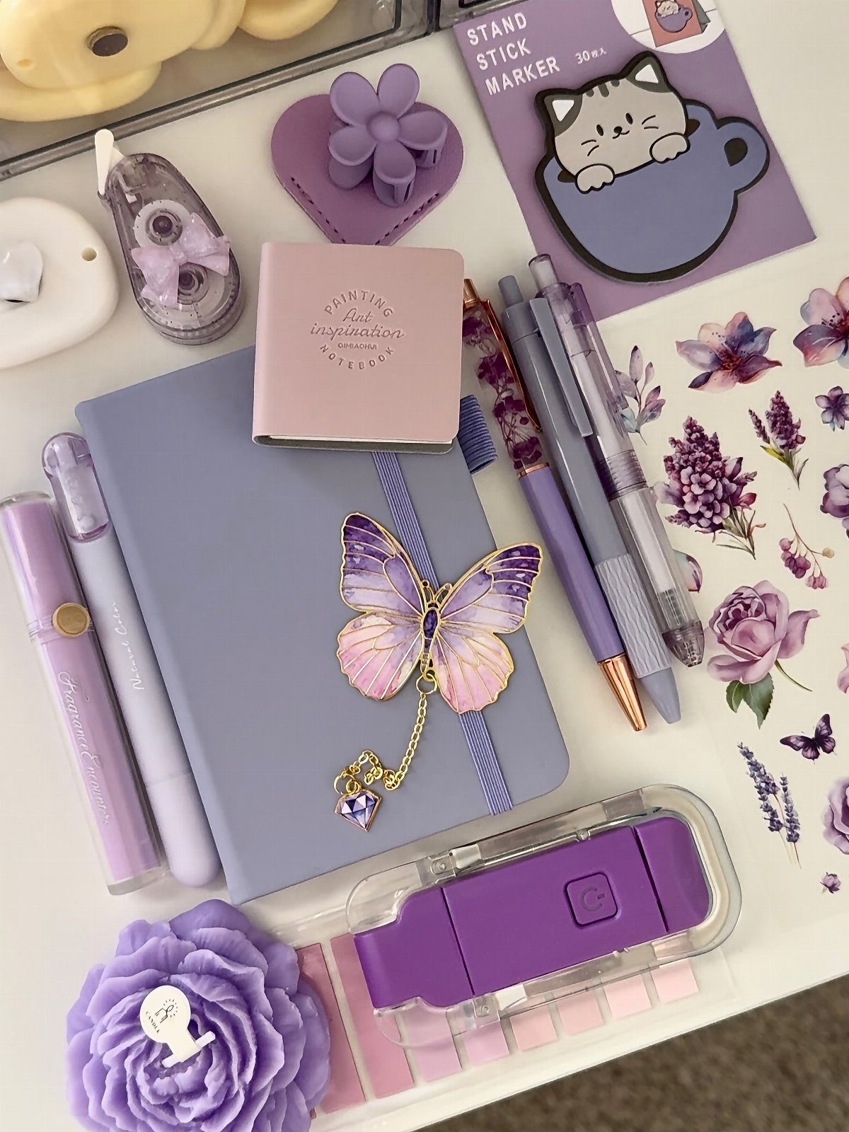 Purple notebook with butterfly charm surrounded by matching pens and stationery accessories.