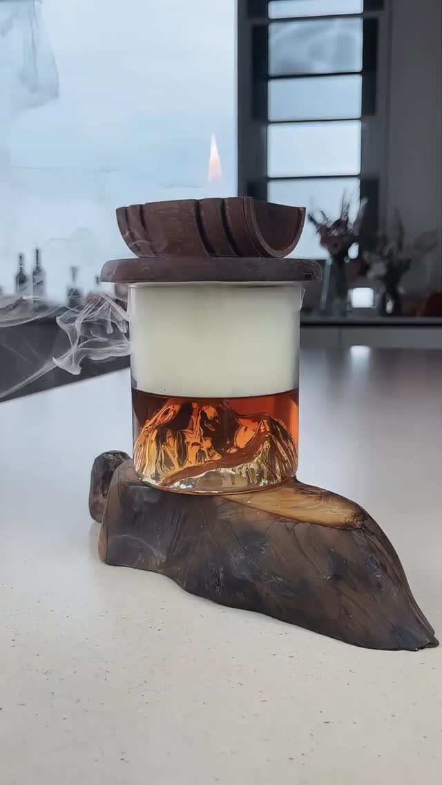 Mountain-shaped glass containing a cocktail with foam, resting on a wooden base.