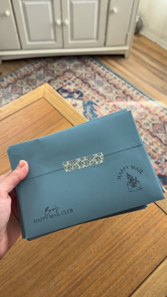 Blue envelope from a happy mail club held over a wooden table.