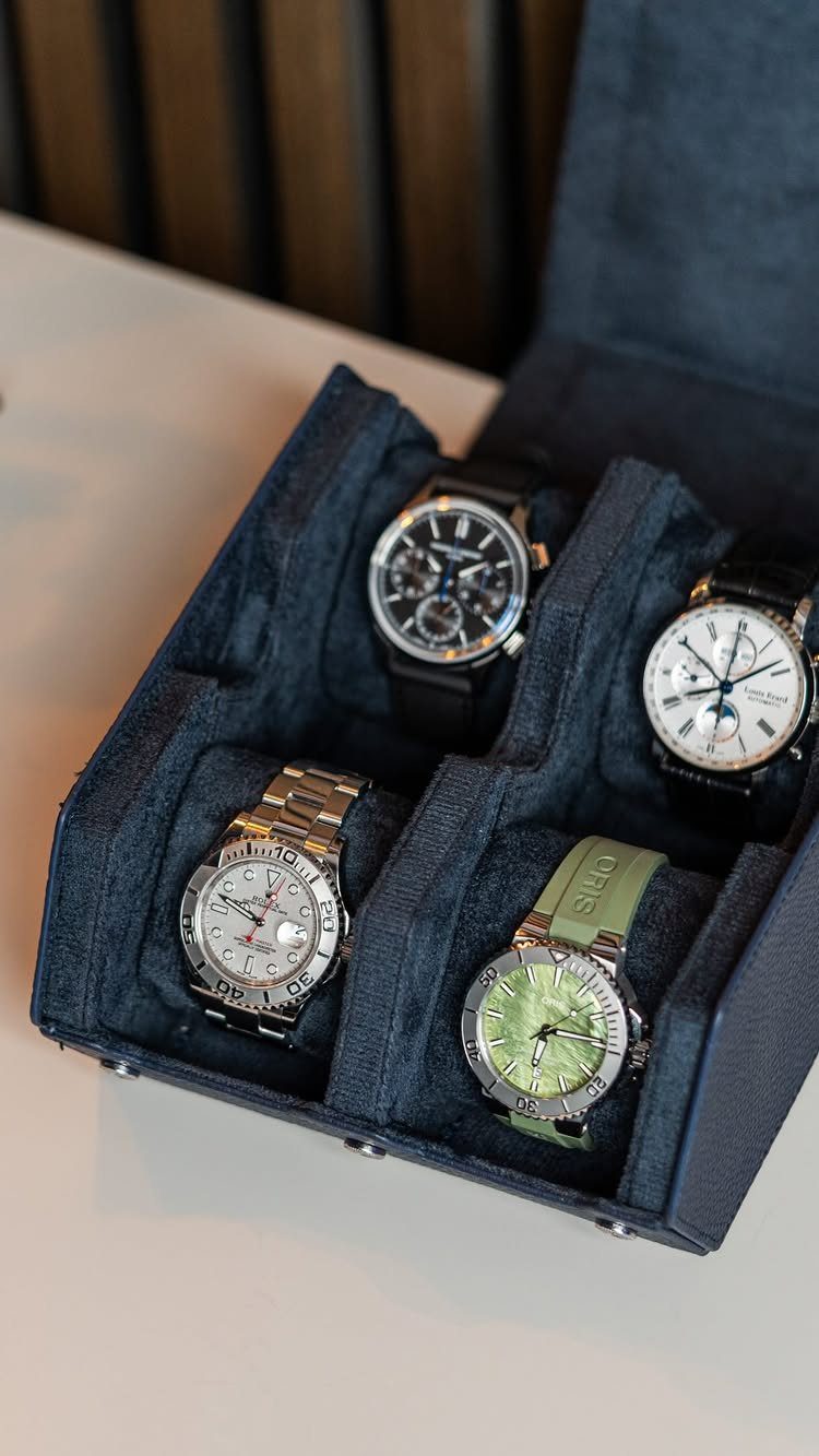 Four wristwatches stored in a dark blue fabric-lined watch organizer box.