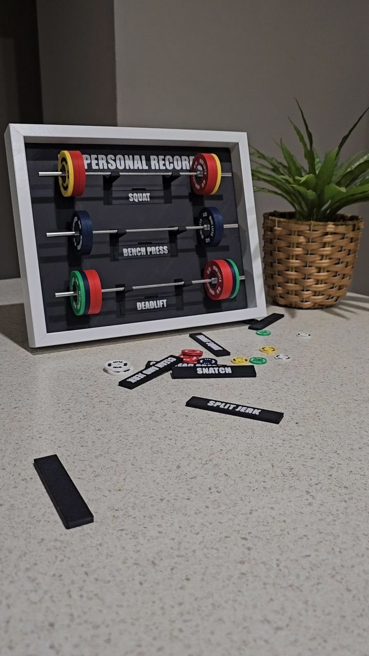 Miniature barbell shadow box for tracking personal records next to a potted plant