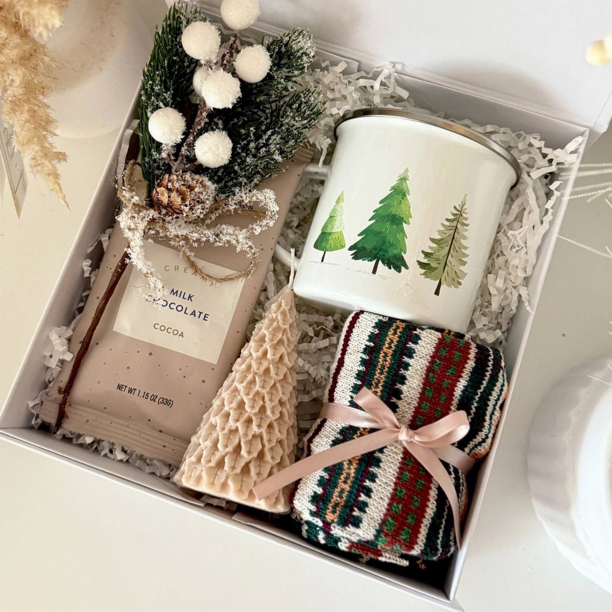Gift box containing chocolate, a pine tree mug, and knitted winter accessories.