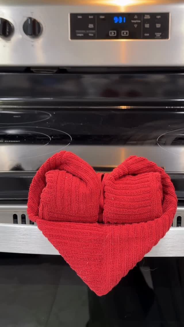 Red knitted heart-shaped pot holder on a black glass stovetop.