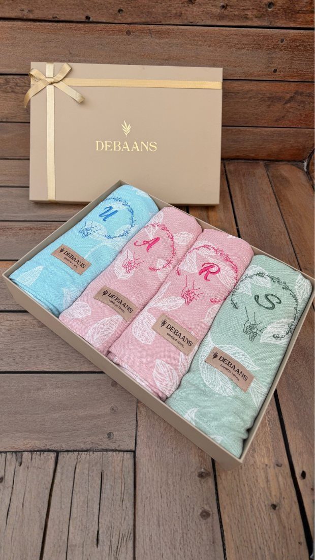 Four embroidered personalized dish towels in pastel colors inside a gift box.