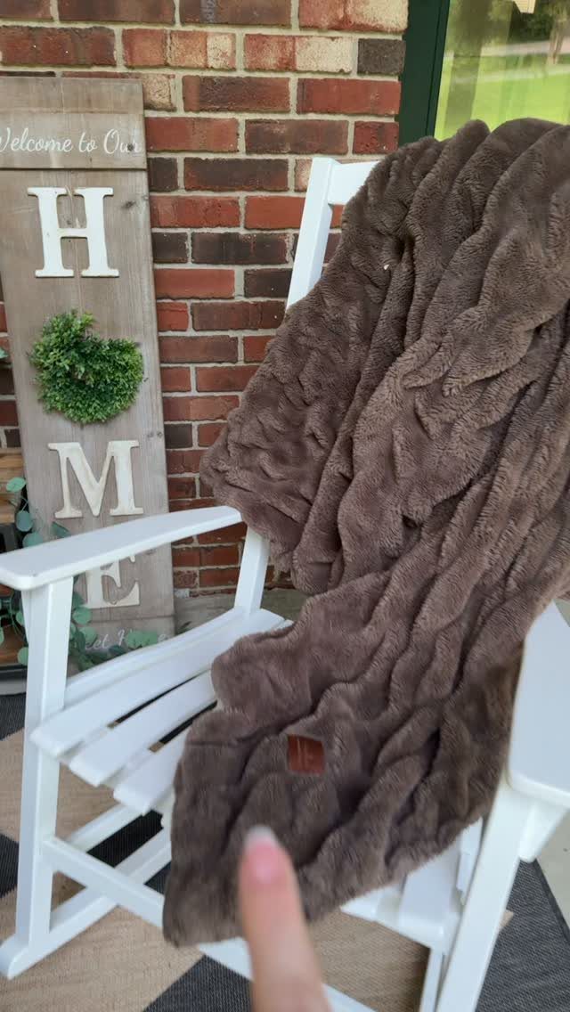 Brown plush blanket draped over a white wooden rocking chair against brick wall