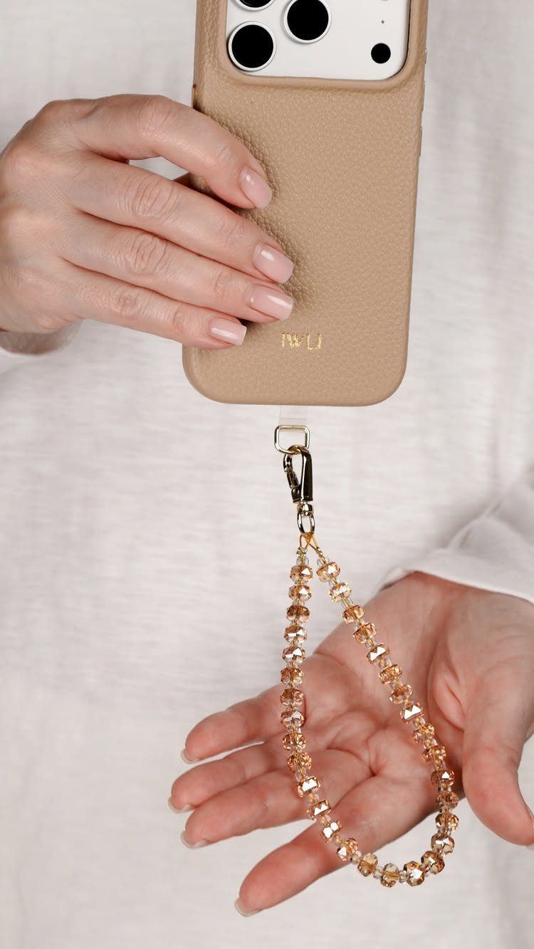 Beige leather phone case with a gold beaded wrist strap held by hands