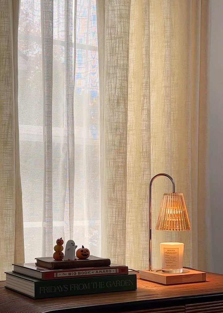 Modern lamp lighting a candle next to books and Halloween figurines by a window