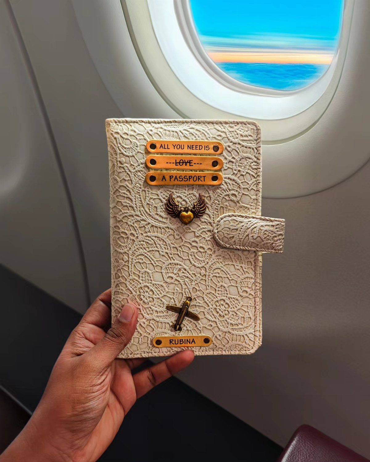 Cream lace passport holder with gold plaques held in front of airplane window