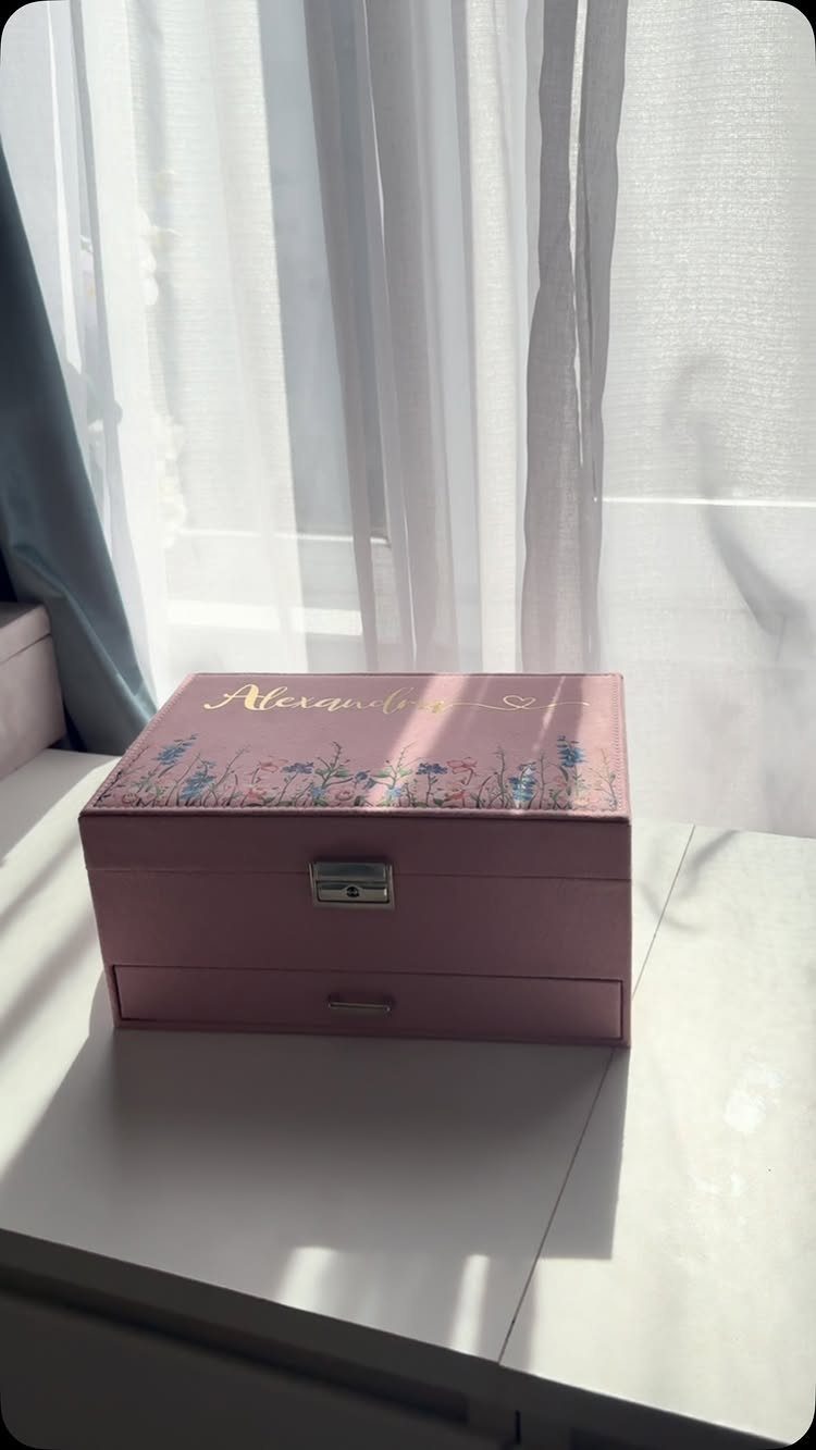 Pink personalized jewelry box with floral design and gold name on white table