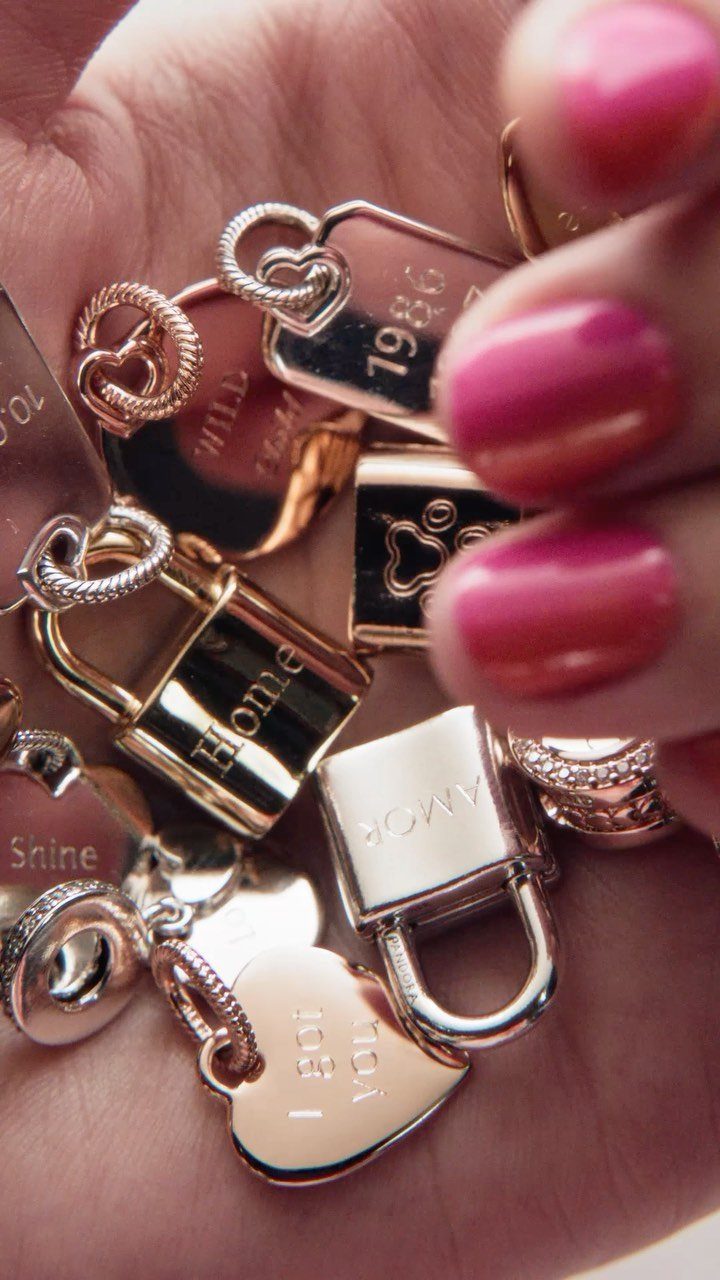 Gold and silver engraved jewelry charms held in a hand with pink nails.