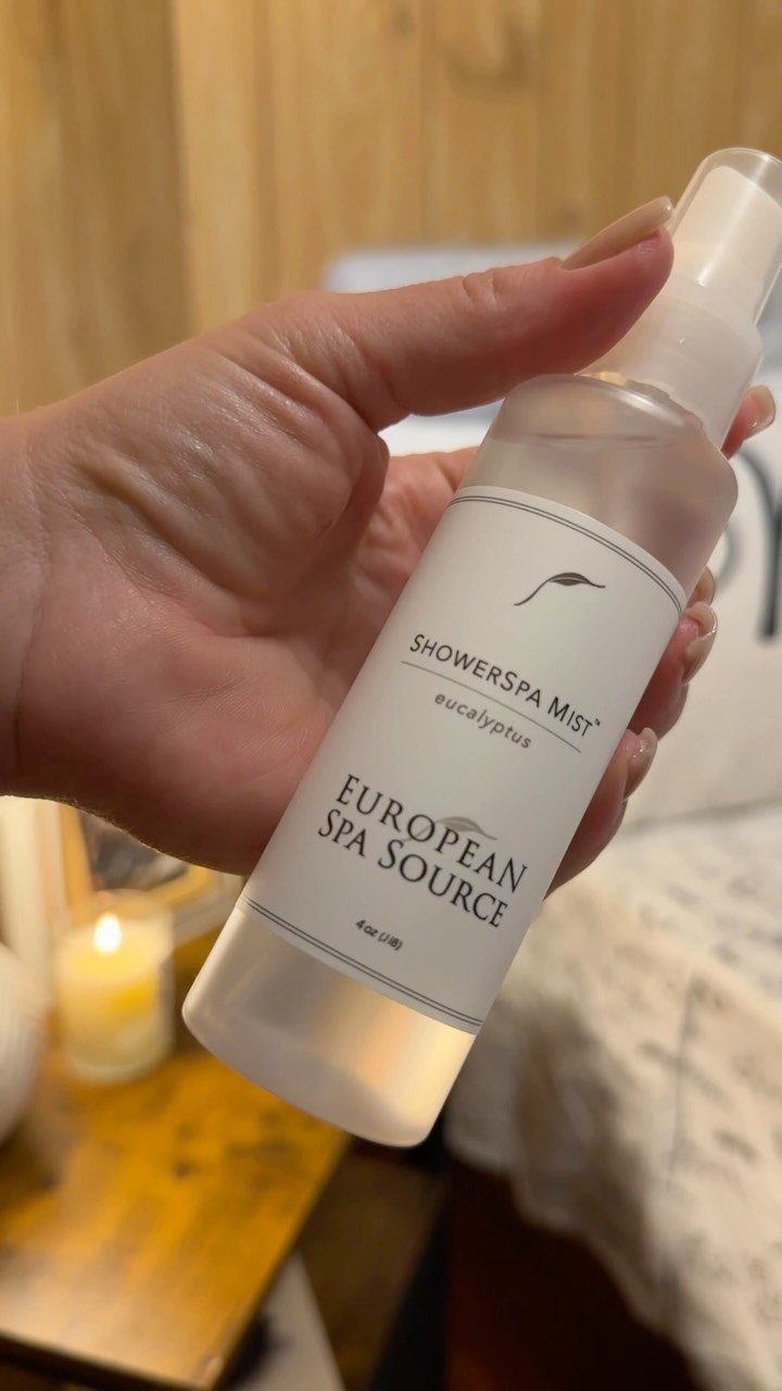 Hand holding a bottle of Eucalyptus ShowerSpa Mist spray in a home setting.