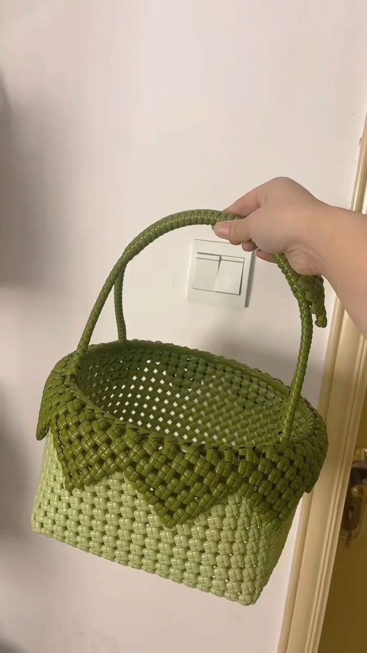 Handmade crochet basket in two shades of green held against a white wall.