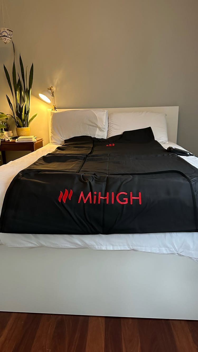 Black MiHIGH infrared sauna blanket spread over a white bed in a bedroom