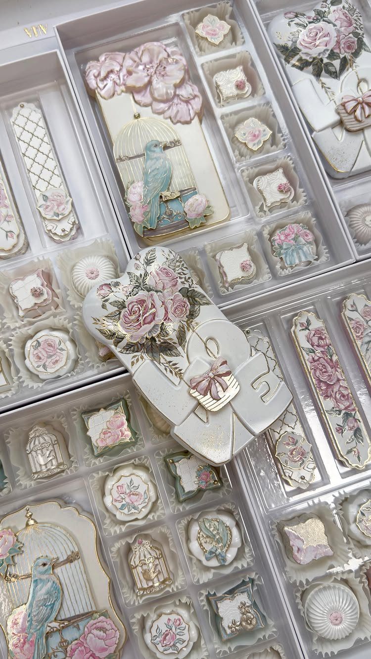 Intricately decorated sugar cookies with pink flowers and birds in white trays.