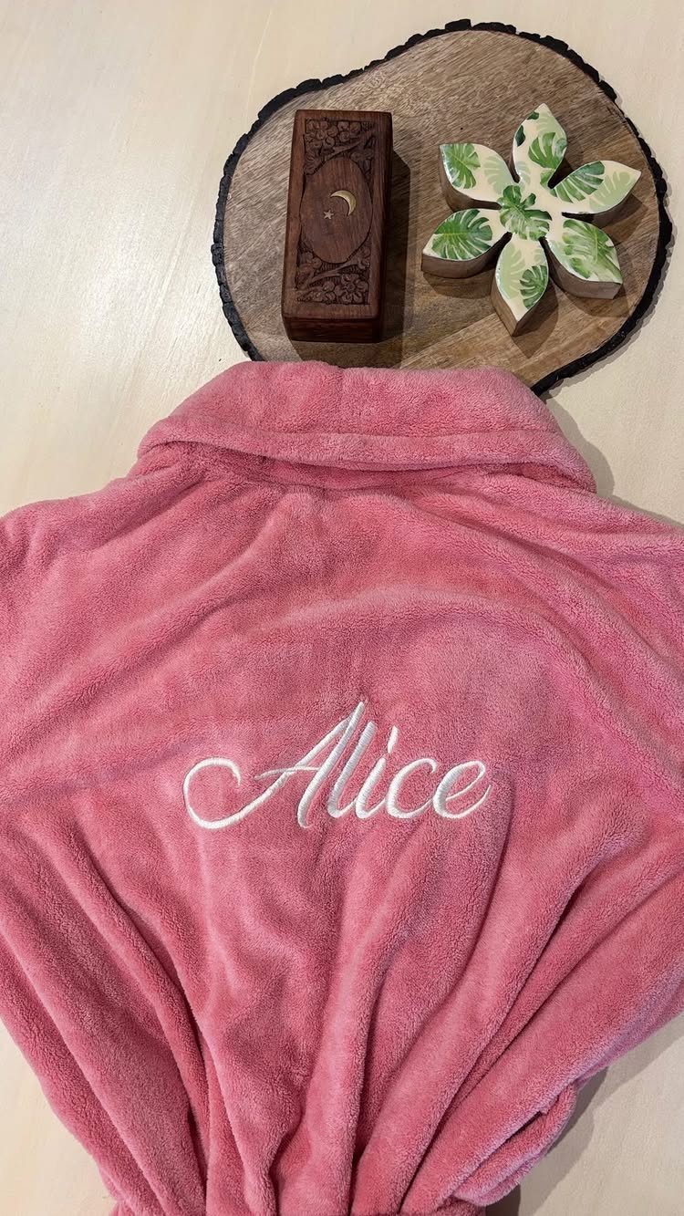 Pink plush bathrobe with Alice embroidered on the back next to handmade soaps.