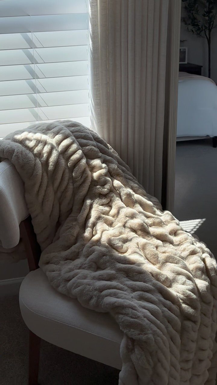 Cream chunky knit throw blanket draped over a white modern chair indoors.