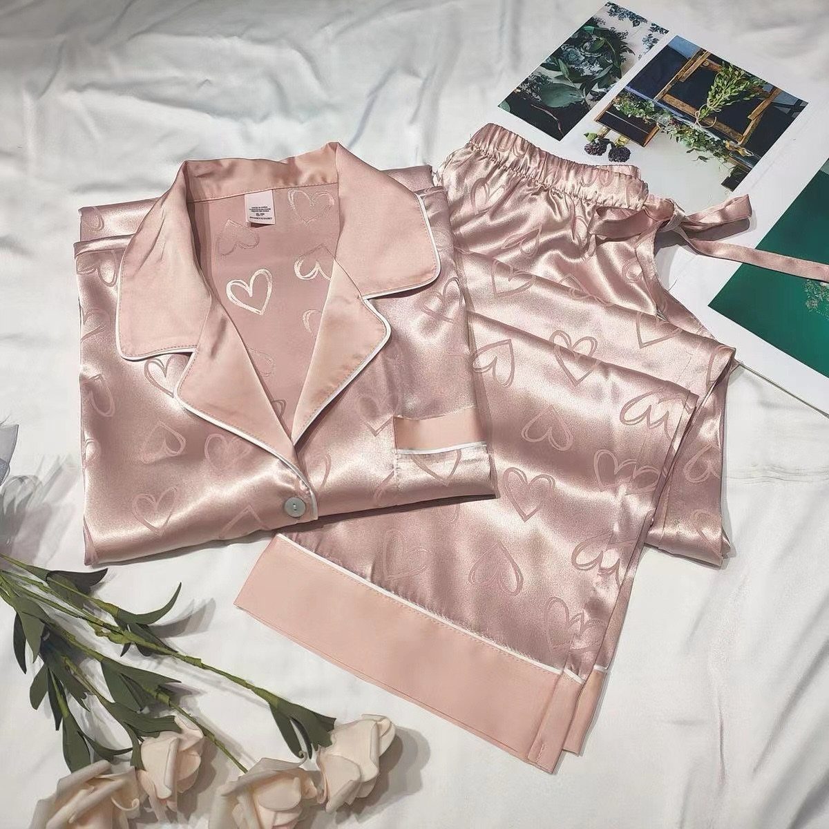 Pink satin pajamas with heart patterns laid on white fabric with white roses.