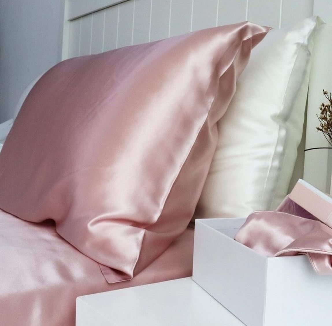 Pink and white silk pillowcases on a bed next to a gift box.