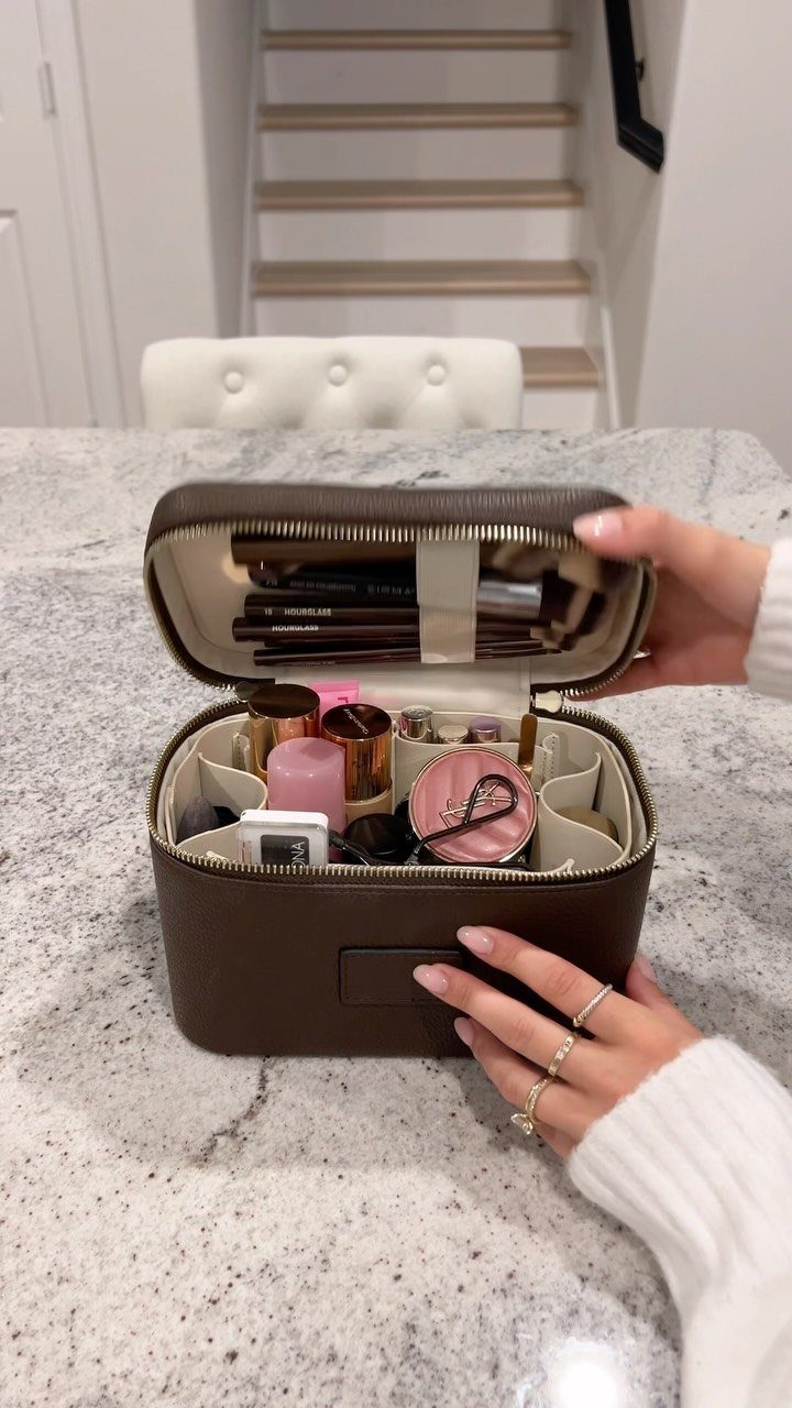 Brown leather makeup bag open and filled with various cosmetics on a countertop.