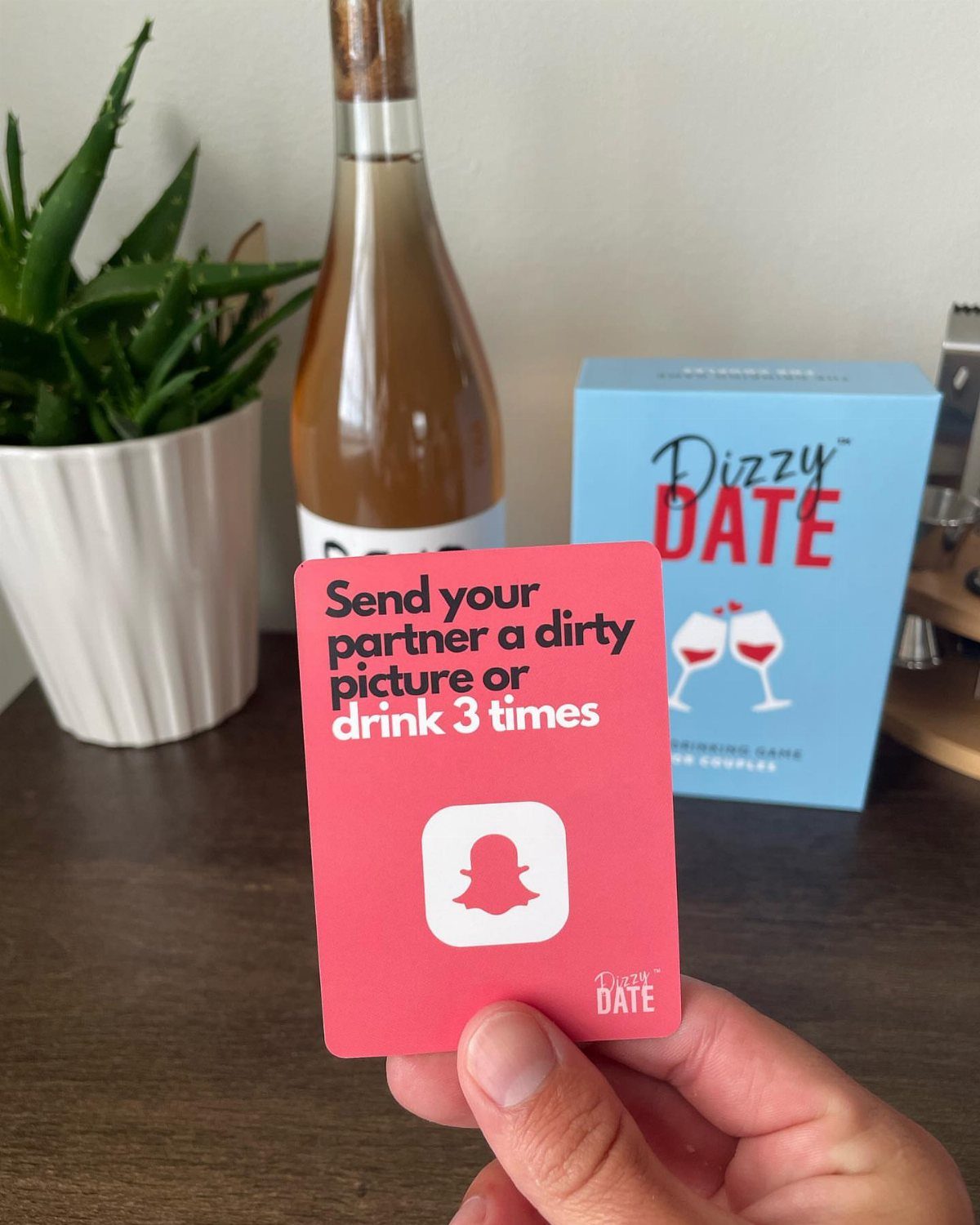 Pink game card held in hand with wine and game box in background
