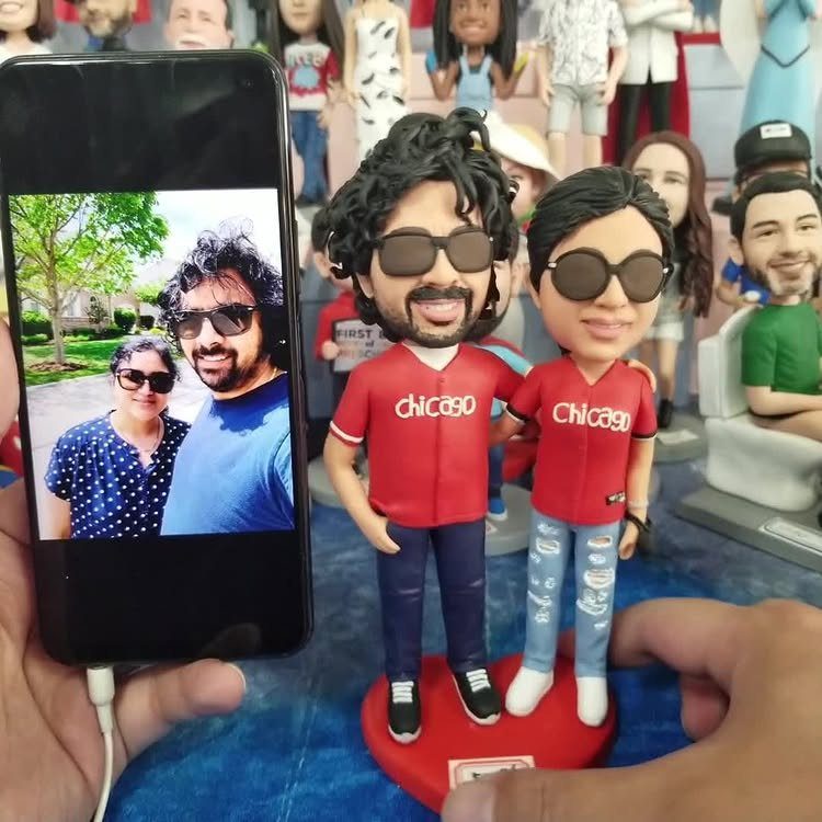 Custom bobblehead couple in red Chicago shirts next to a reference photo on smartphone