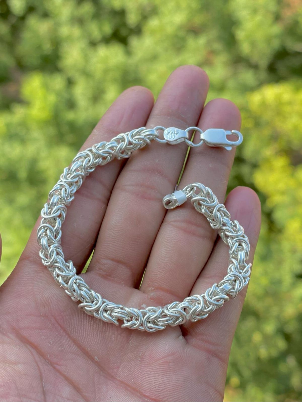 Silver woven link chain bracelet held in a person's open palm outdoors.