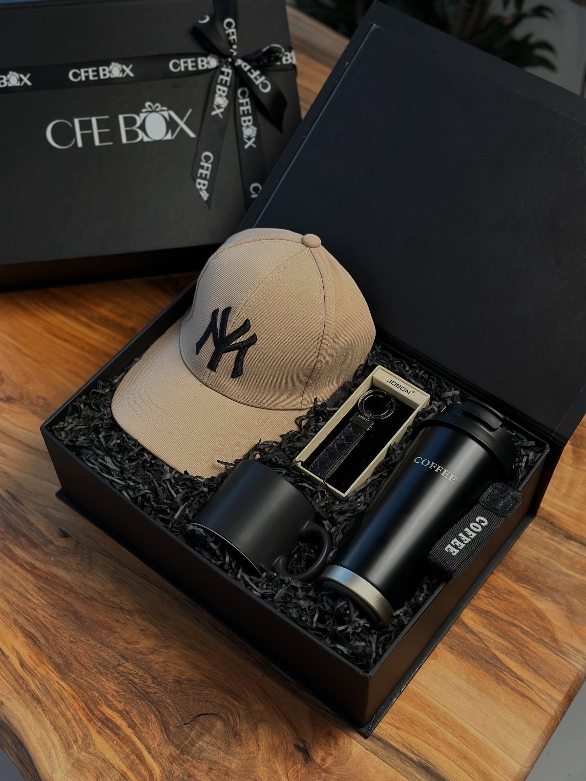 Gift box with tan baseball cap, black coffee mug, and travel tumbler.