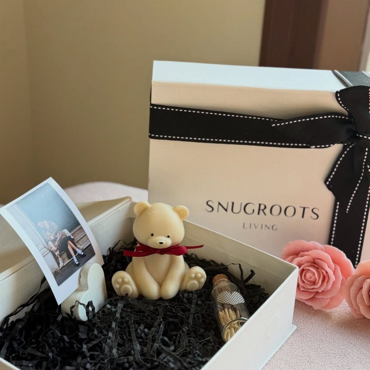 Gift box with a small teddy bear, a couple's photo, and a tiny bottle.