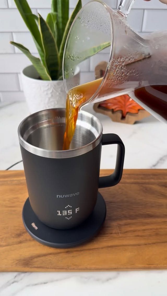 Black temperature-controlled mug on a heating coaster with coffee being poured in.