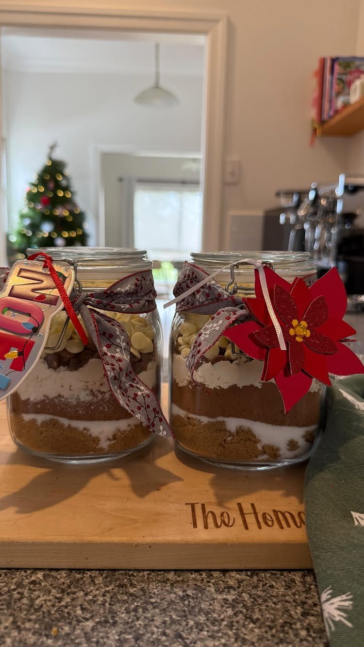 Two mason jars with layered brownie mix, decorated with ribbons and a poinsettia.