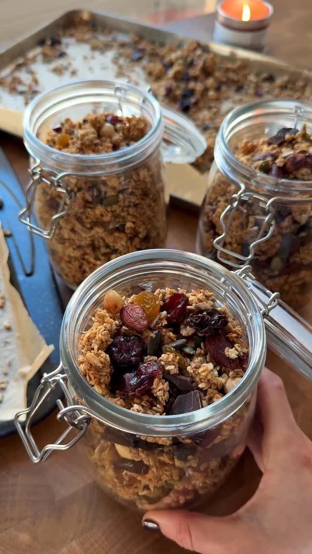 Glass jars filled with homemade granola, dried berries, and chocolate on wooden table