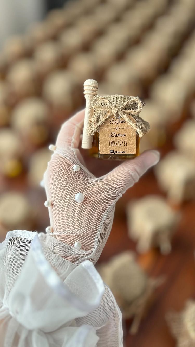 Small glass jar of golden honey with burlap topper held by gloved hand