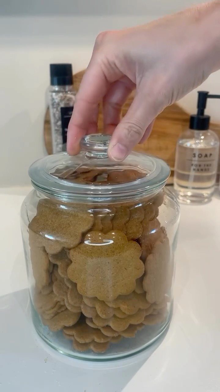 Glass jar filled with flower-shaped cookies on a white counter with a hand reaching.