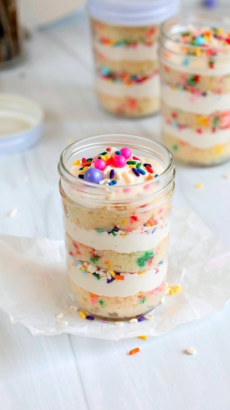 Layered cake and frosting dessert in a mason jar topped with colorful sprinkles