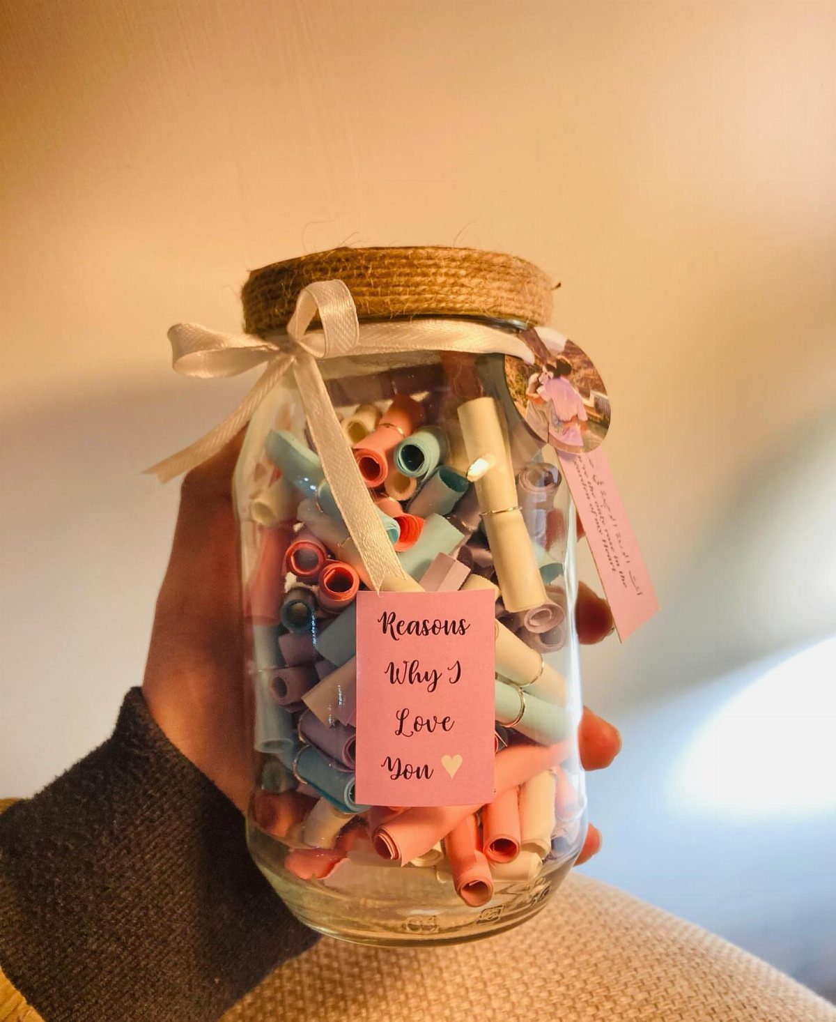 Mason jar filled with colorful rolled paper notes and a white ribbon bow.