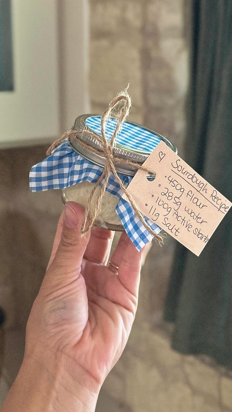 Hand holding a mason jar with a checkered lid and sourdough recipe tag.