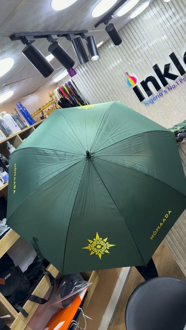 Open dark green umbrella with yellow logo and text in a shop setting