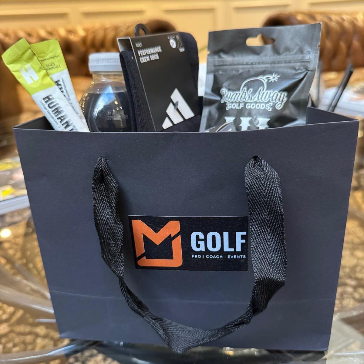 Black golf gift bag filled with socks, water, and golf accessories.