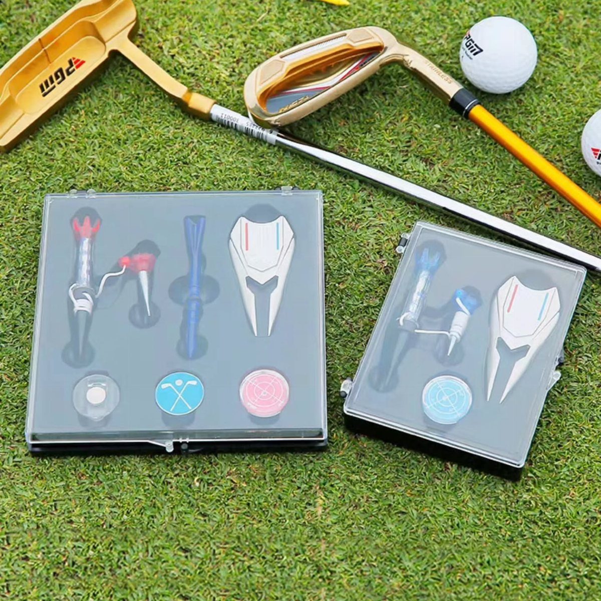 Golf gift sets in clear cases with accessories on green grass with clubs.