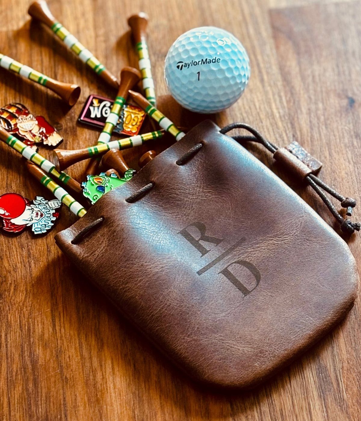 Brown leather personalized valuables pouch with golf ball, tees, and ball markers.