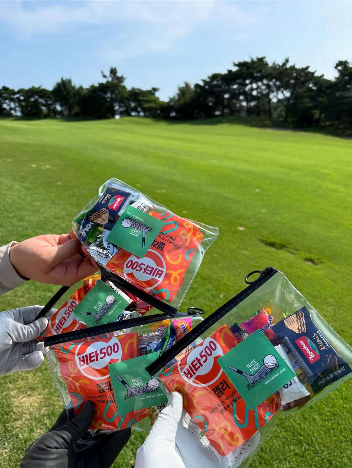 Clear zipper pouches filled with snacks and golf stickers on a golf course.
