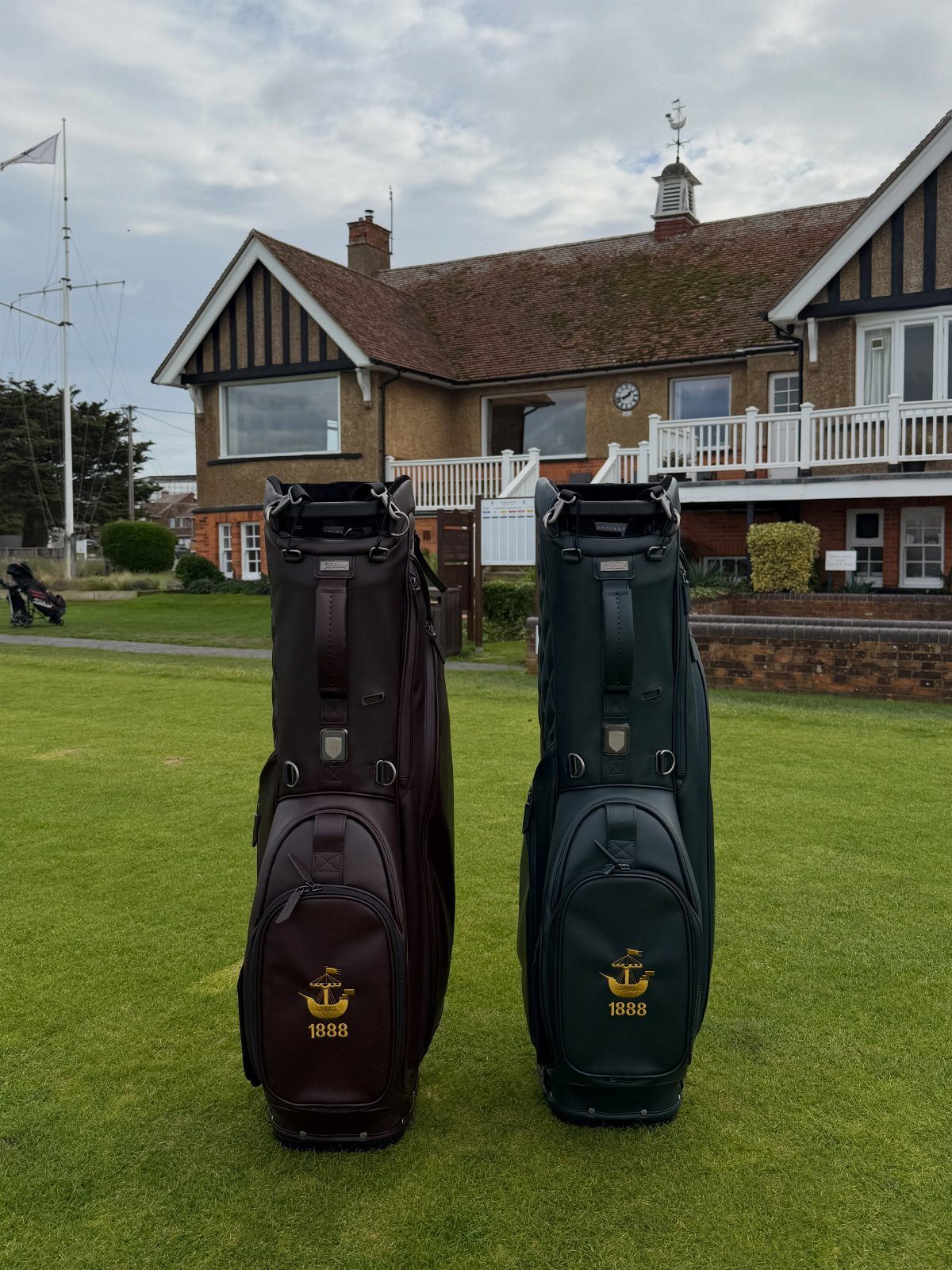 Two luxury golf bags in brown and green standing on a golf course lawn.