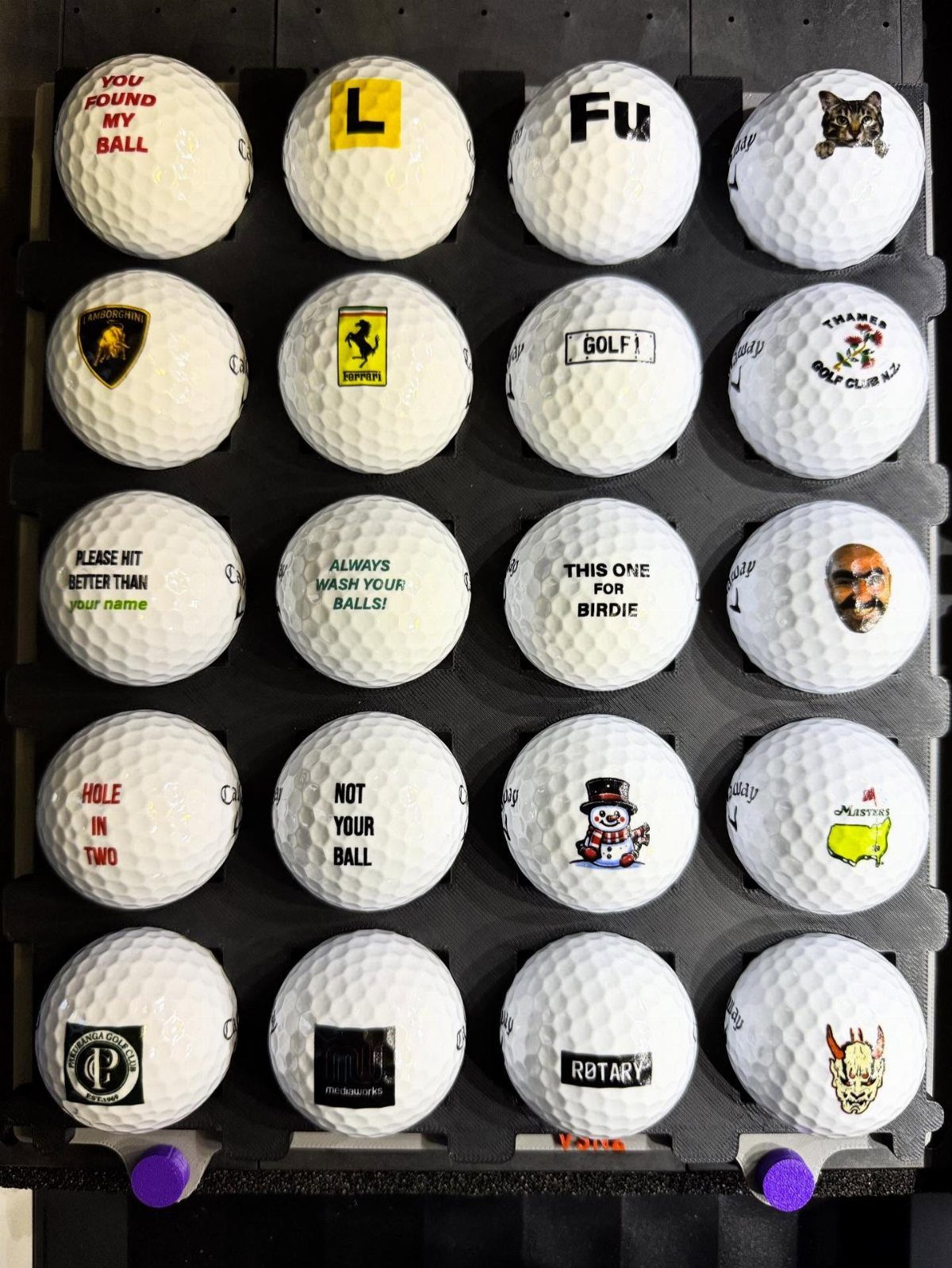 White golf balls with various personalized logos and text in a black display grid