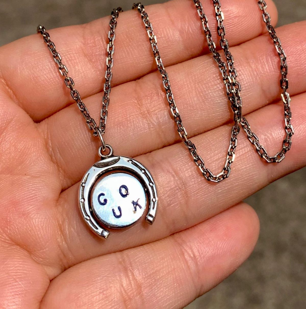 Silver horseshoe necklace with engraved text held in a person's open palm.
